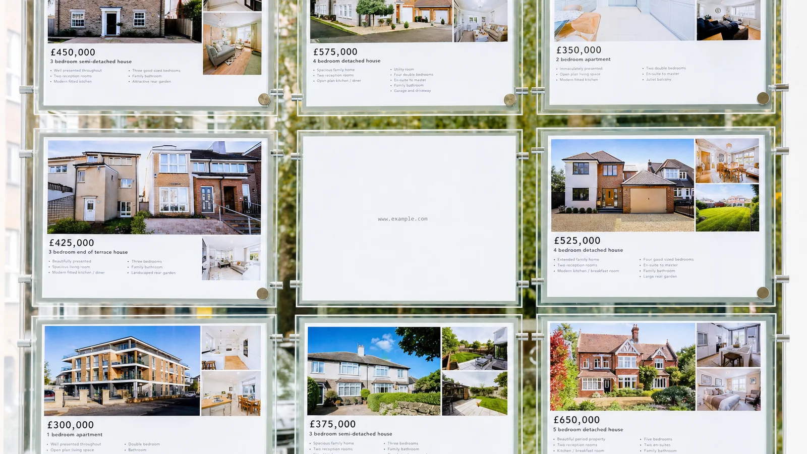 A bright estate agent window full of detailed colourful property cards, with one completely blank white card in the centre showing only a small web address.
